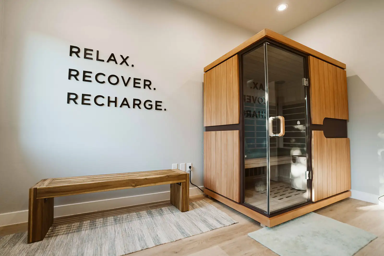 Sunlighten sauna beside a bench and Relax Recover Recharge wall lettering